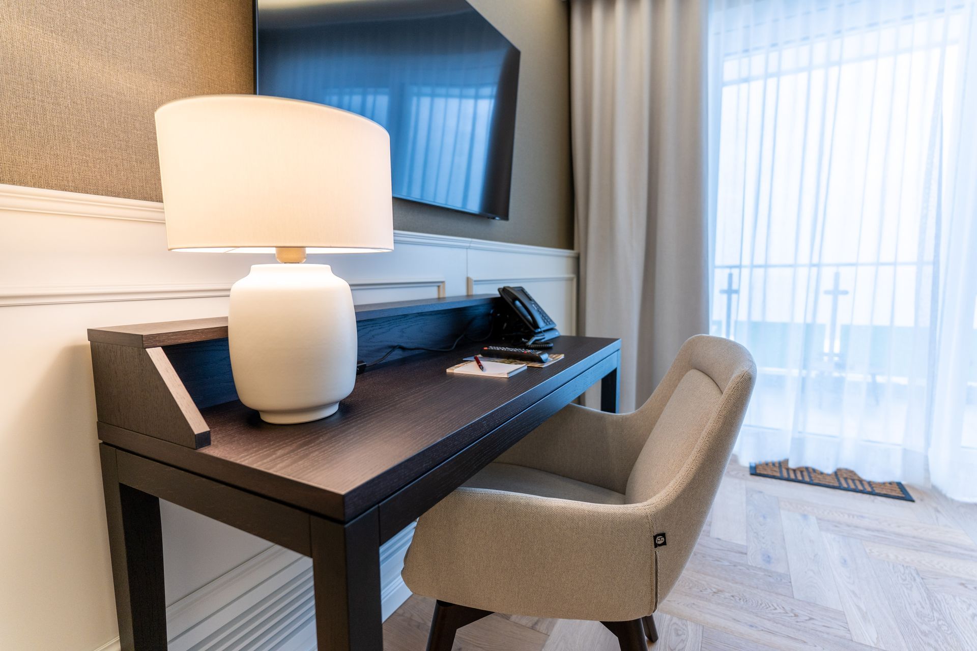 Ein Schreibtisch mit einer Lampe und einem Stuhl in einem Hotelzimmer.