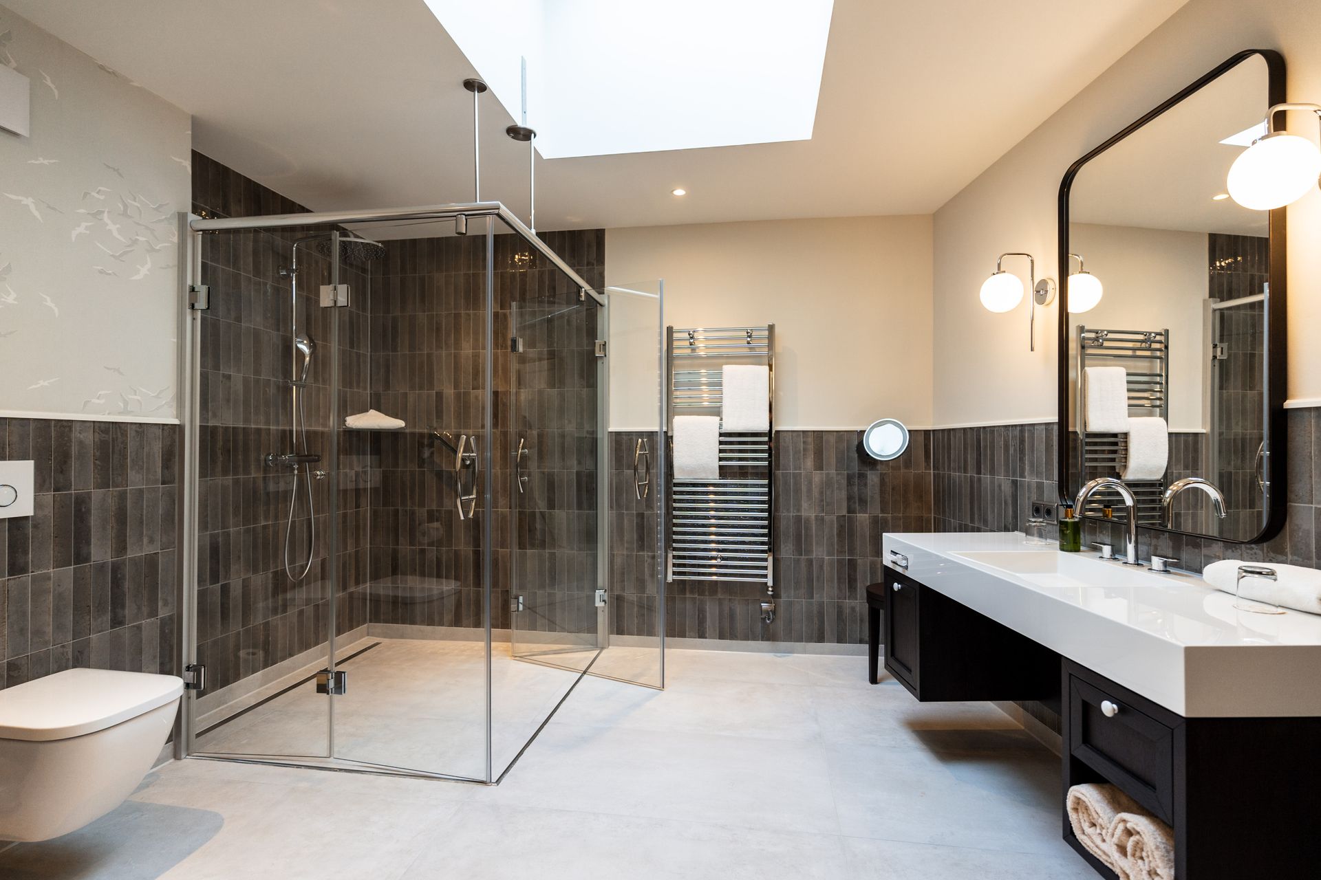 Ein Badezimmer mit ebenerdiger Dusche, Waschbecken, Toilette und Spiegel.