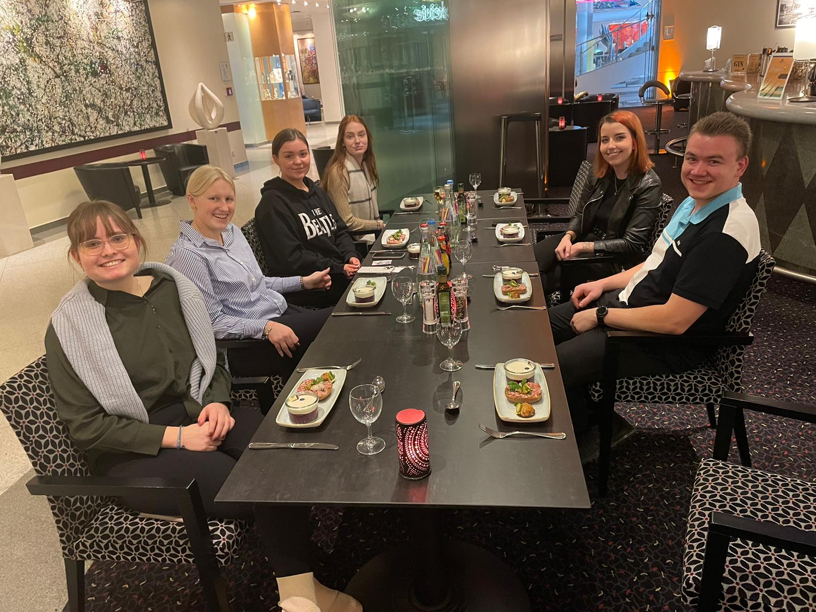 Eine Gruppe von Menschen sitzt um einen Tisch herum, auf dem Teller mit Essen stehen.
