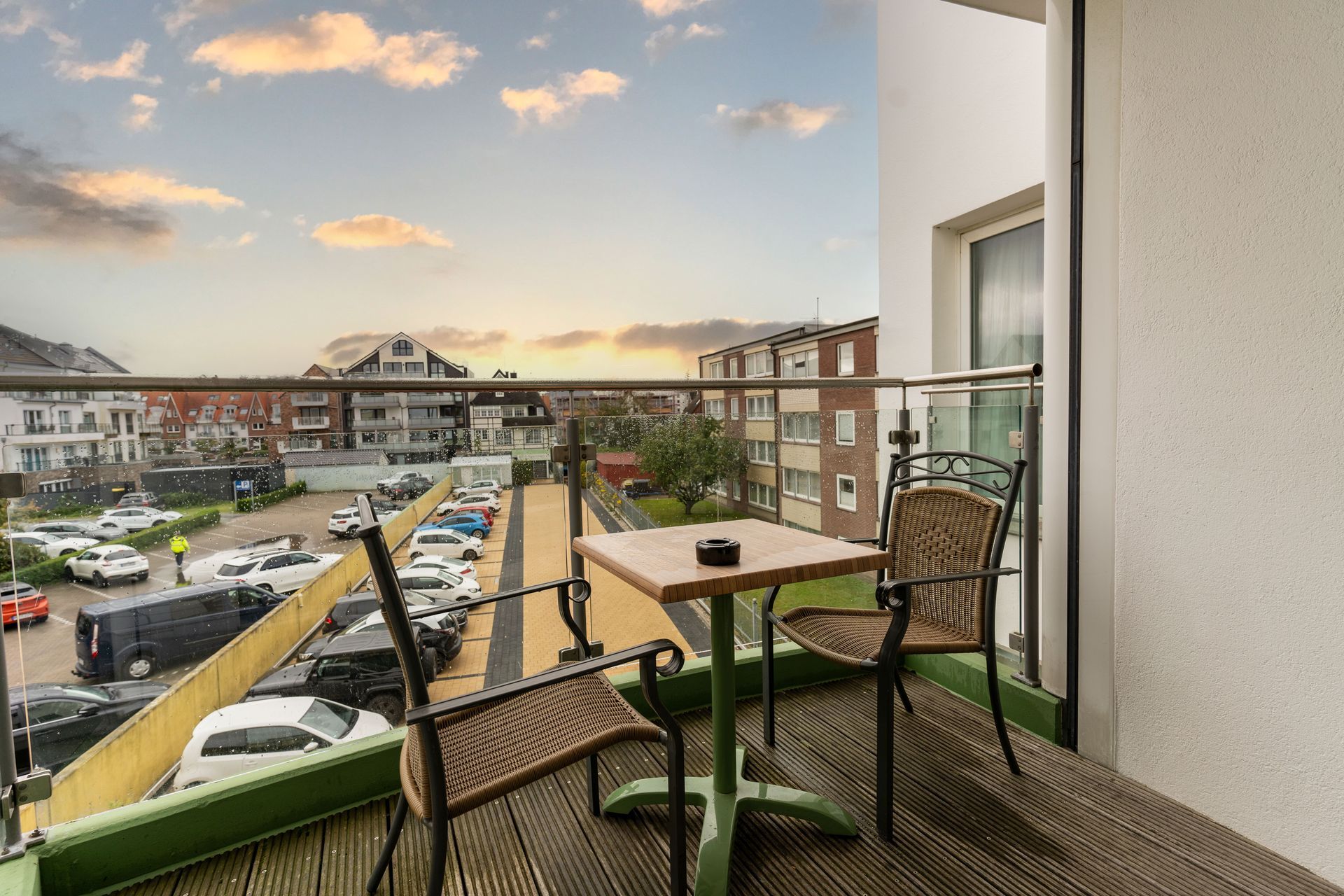 Ein Balkon mit Tisch und Stühlen mit Blick auf einen Parkplatz.