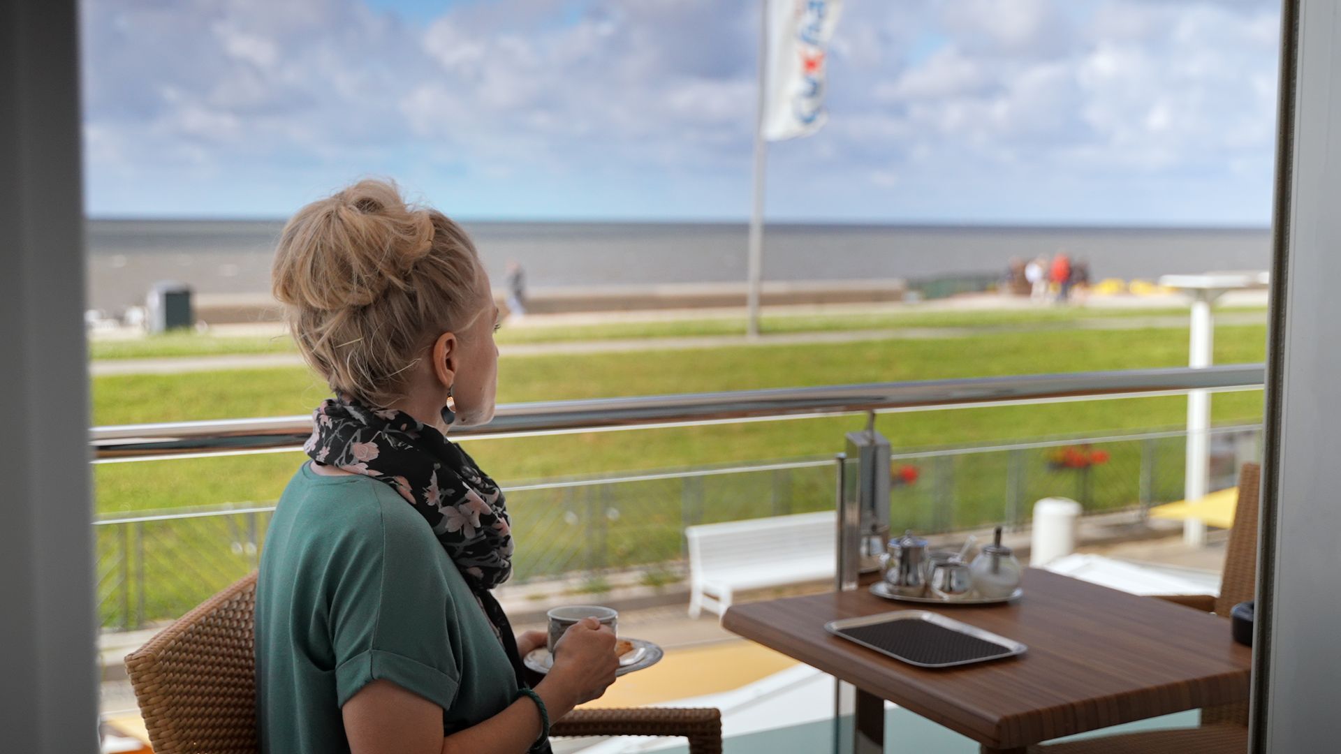 Eine Frau sitzt an einem Tisch und schaut aus dem Fenster auf das Meer.