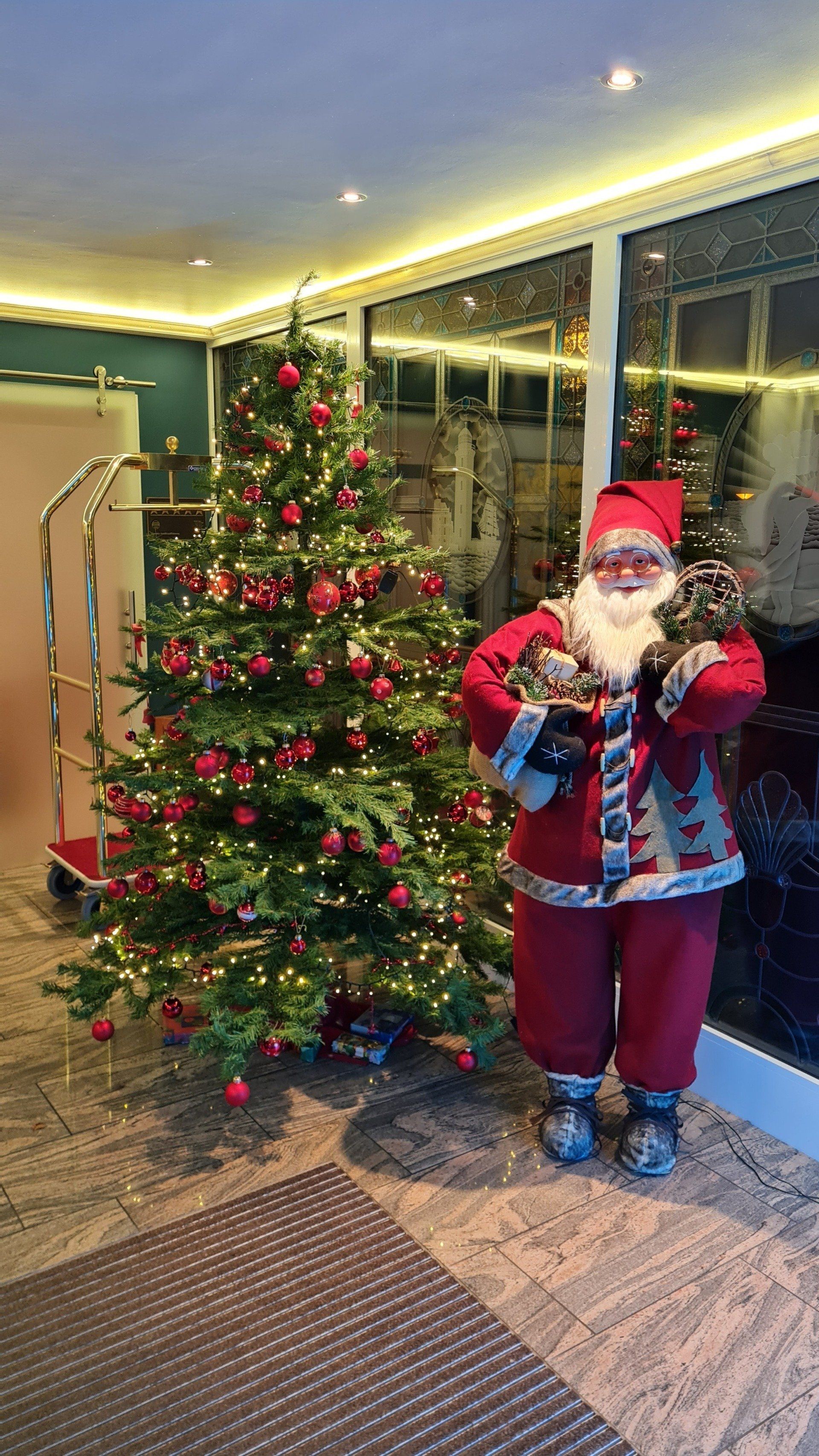 A santa claus statue is standing in front of a christmas tree.