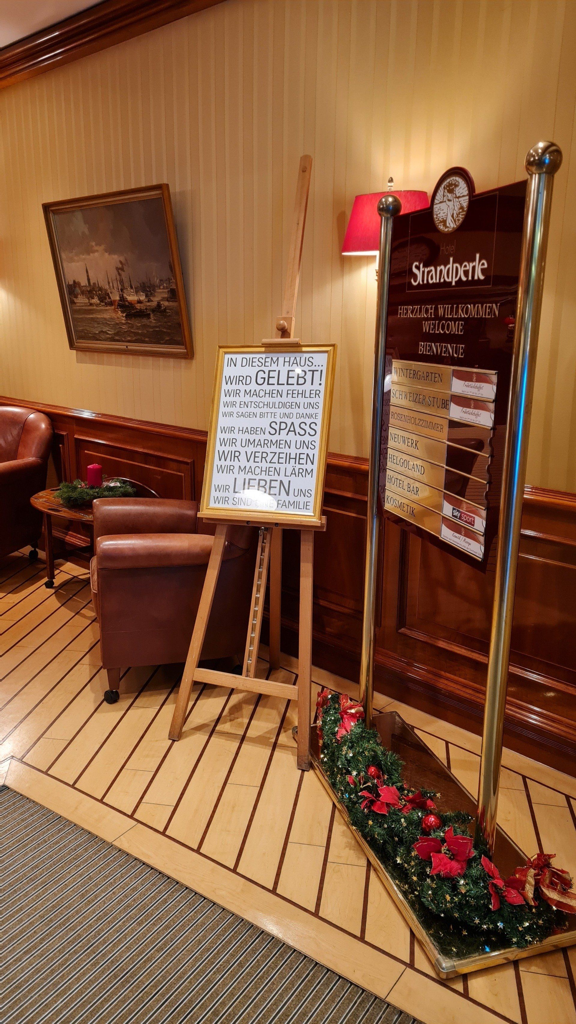 A sign on an easel in a room with chairs and a clock.
