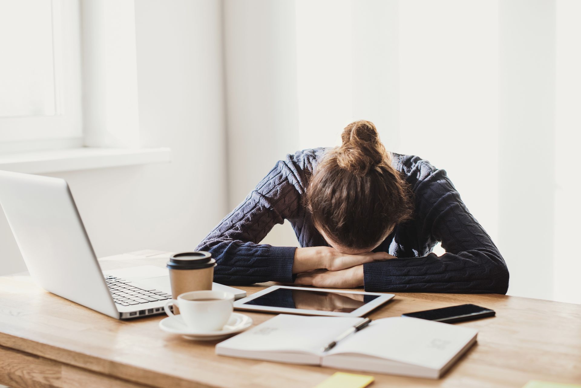 A woman is sitting at a desk with her head in her hands.