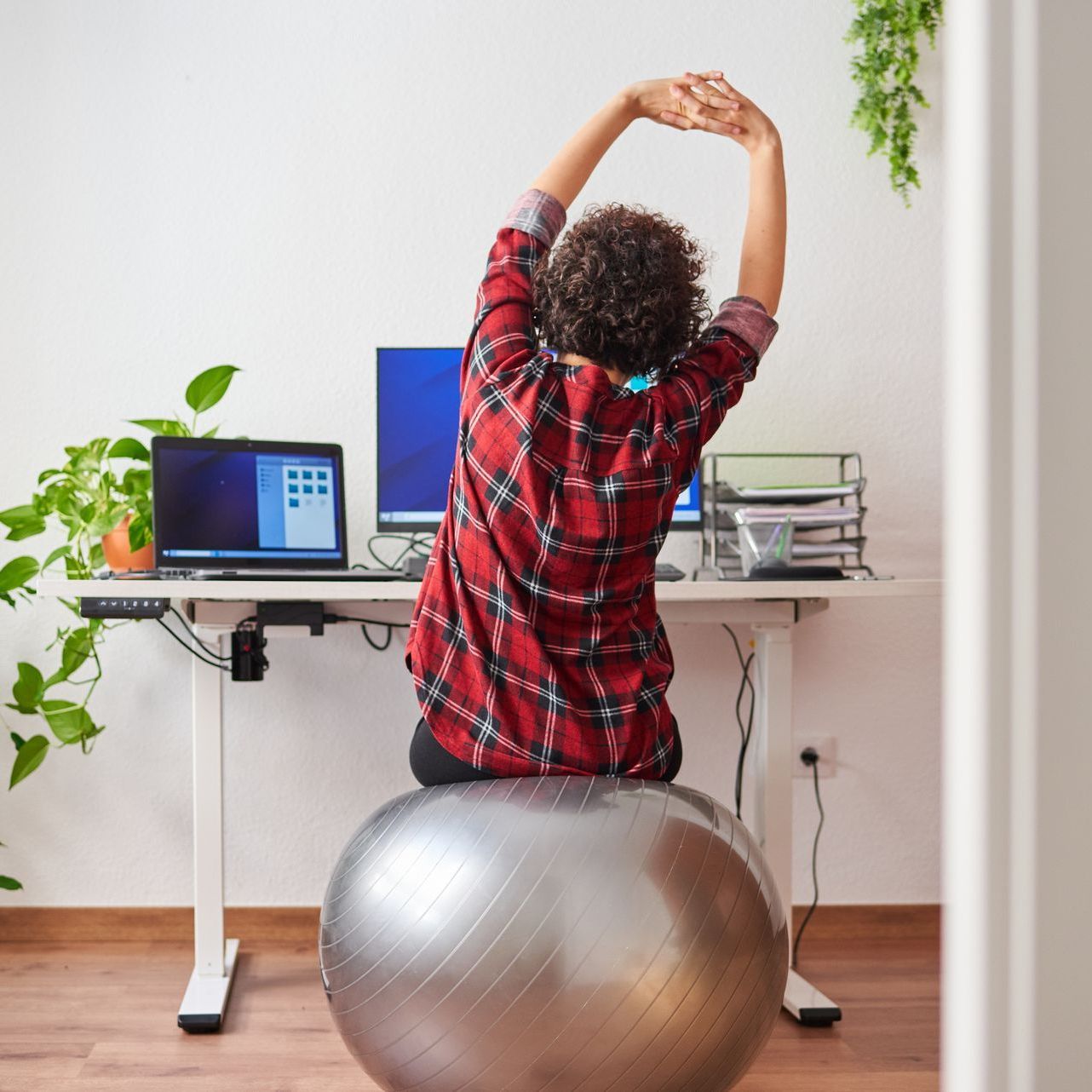 A woman is sitting on an exercise ball in front of a desk.