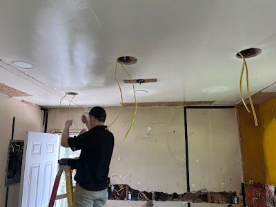 A man is standing on a ladder working on the ceiling of a room.
