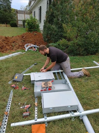 A man is kneeling down in the grass working on a electrical box.