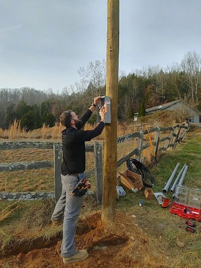 A man is standing next to a wooden pole in a field.