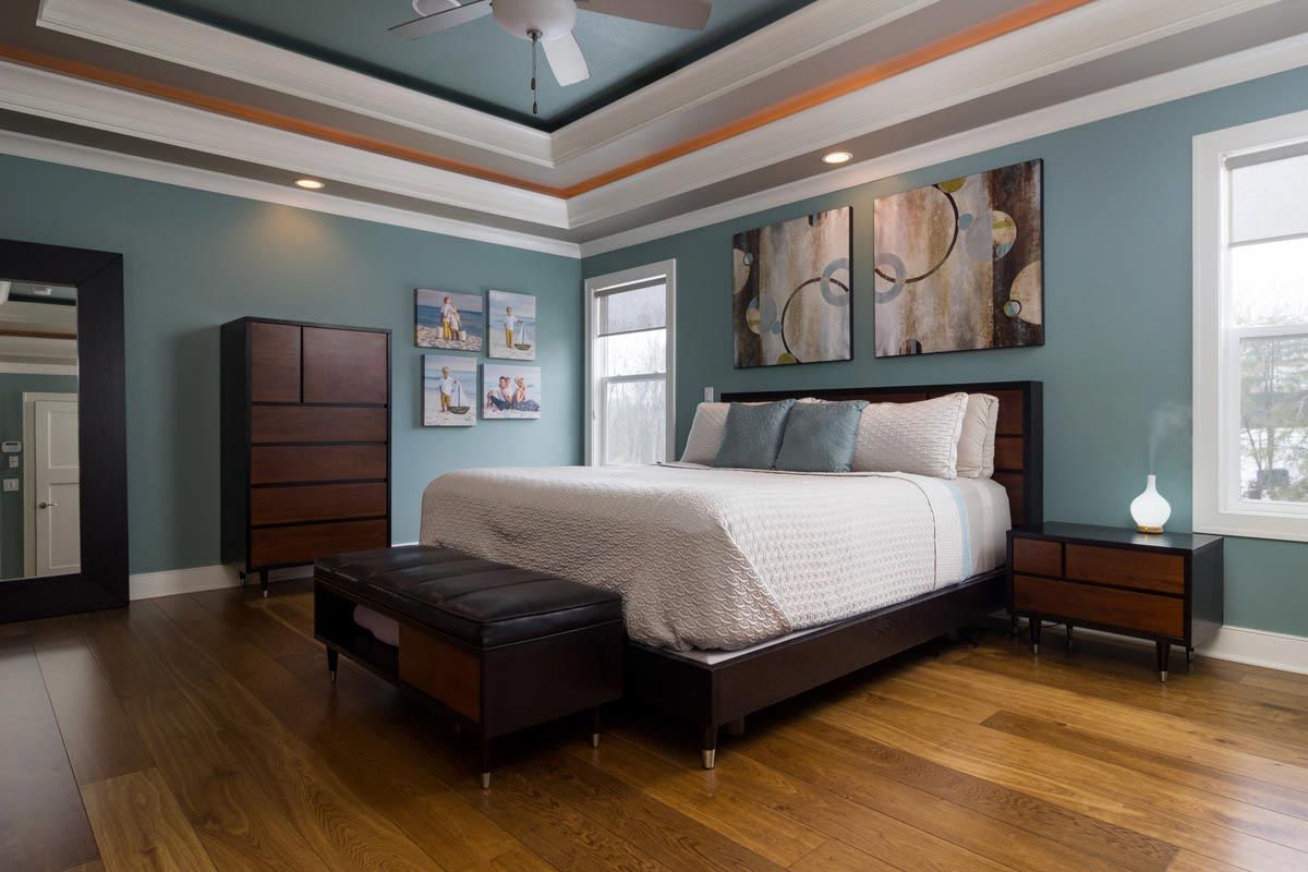 Bedroom with blue walls, wood furniture, and a king-sized bed. Artwork and a dark floor.