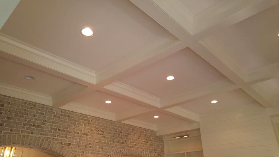 White coffered ceiling with recessed lighting above brick wall.
