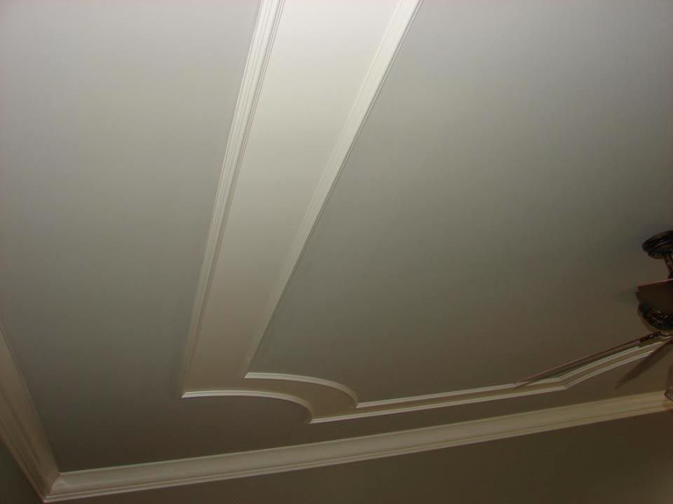 White ceiling with decorative molding in a room. A ceiling fan is visible in the corner.