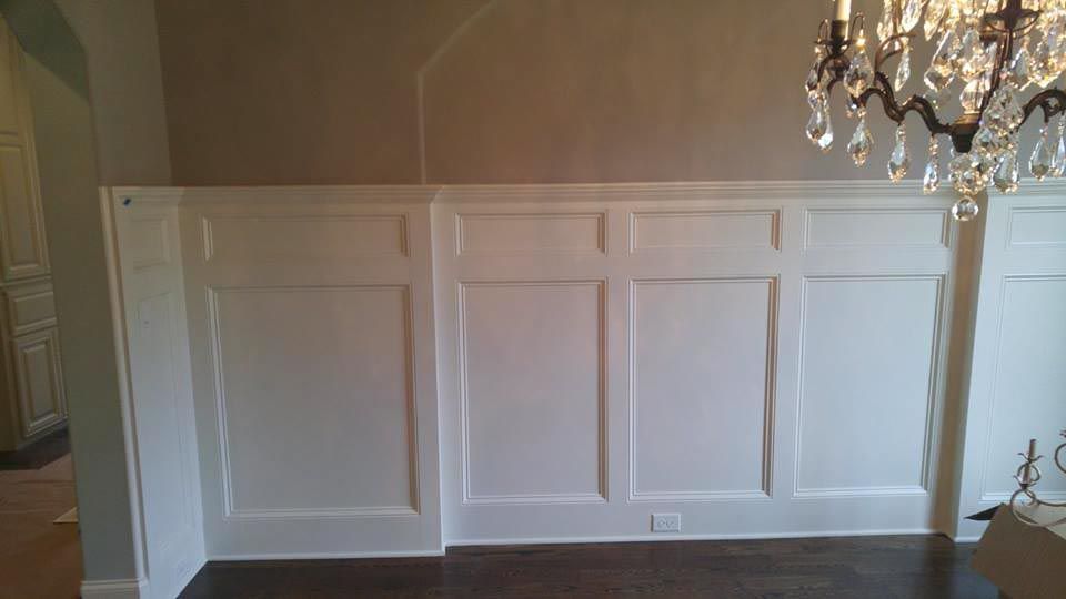 White paneled wall with a dark floor and chandelier hanging on the right.