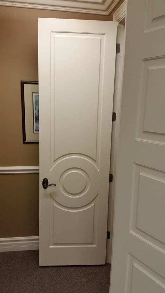 White door with black handle and decorative circular panel, open slightly in a room with a painting.
