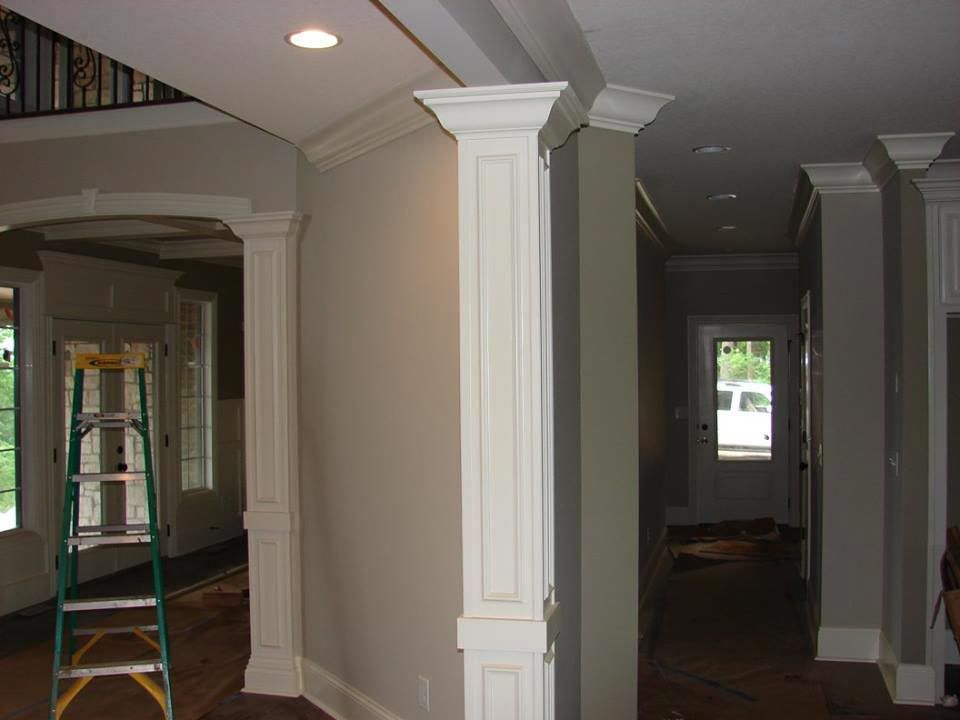Interior hallway with white pillars, crown molding, and ladder.