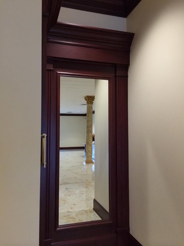 Doorway with dark wood trim and a full-length mirror, reflecting a hallway with a pillar and light-colored flooring.