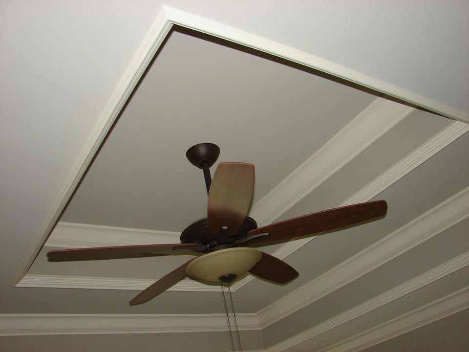 Ceiling fan with wooden blades in a recessed ceiling with crown molding.