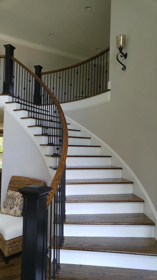 Curved wooden staircase with black railing and white risers in a home setting.