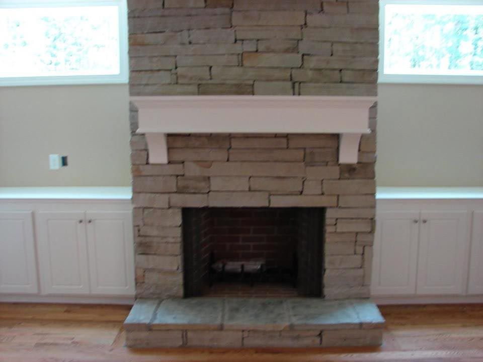 Stone fireplace with white mantel, flanking white cabinets, two windows above.