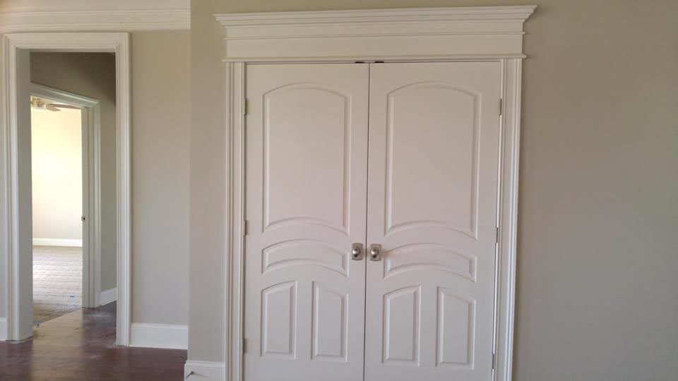 White double doors with decorative top molding, flanked by a doorway and painted walls.