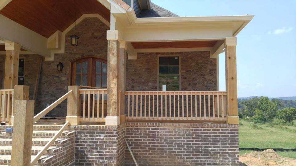 Brick home exterior with porch, wooden posts, railings, and steps.