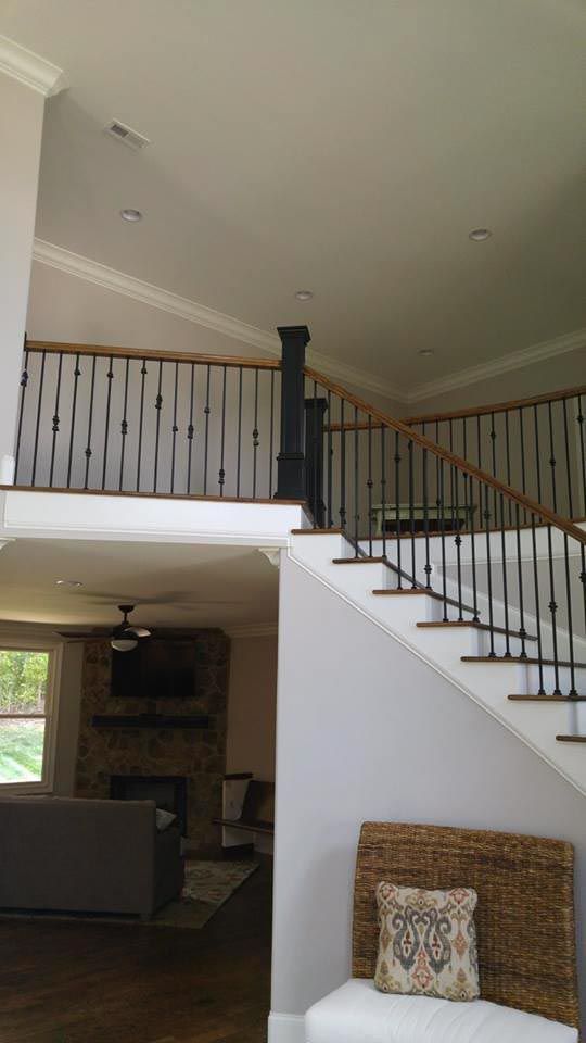 Interior view: stairwell with black iron railings, white walls, and a view of a living room with a fireplace.