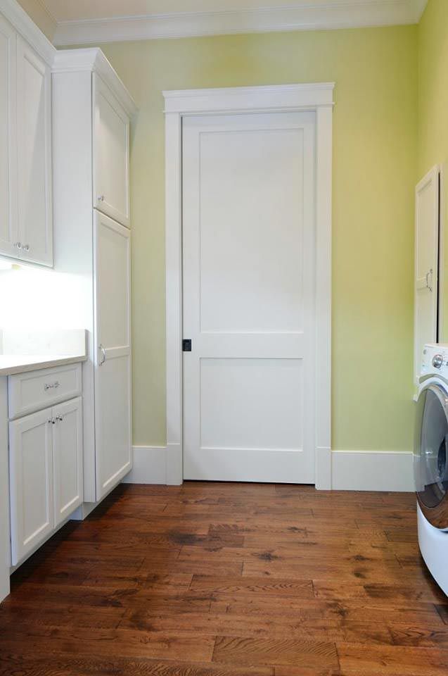 Laundry room with white cabinets, door, and washer against light green walls, brown floor.