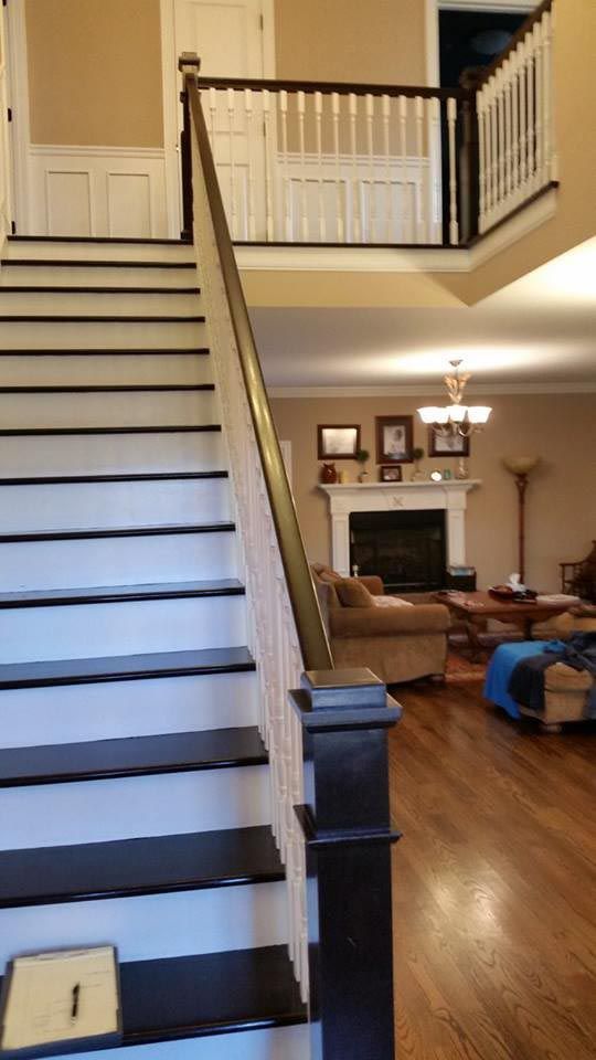 Staircase with black treads, white risers, and a brown banister leads to a second-floor landing with a railing.