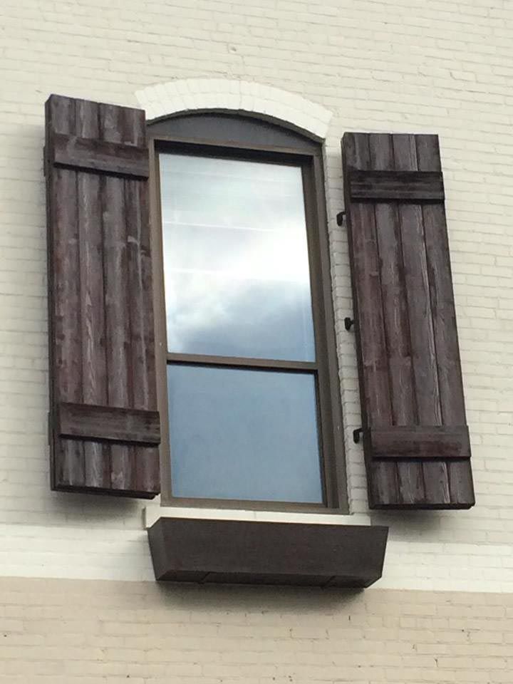 Window with open wooden shutters on a light brick wall, a brown window frame and a matching window box below.