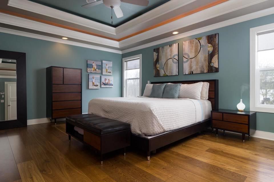 Bedroom with blue walls, hardwood floor, bed with large art, and dark wood furniture.
