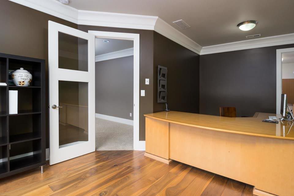 Office with brown walls, wood floor, glass door, and wooden desk.