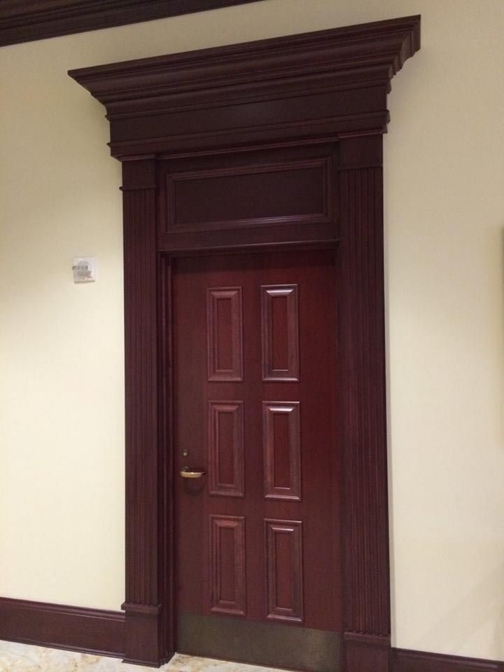 Dark wood door with paneled design and matching ornate trim, set in a cream-colored wall.