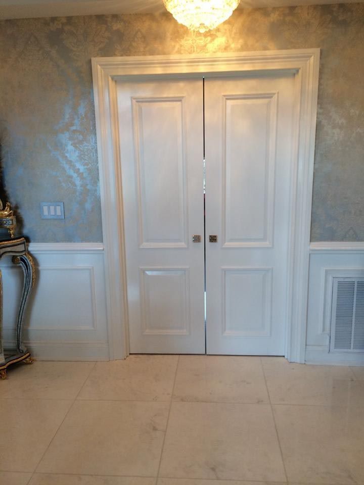 White double doors framed by trim, beneath a decorative light fixture, set against a shimmering wall.