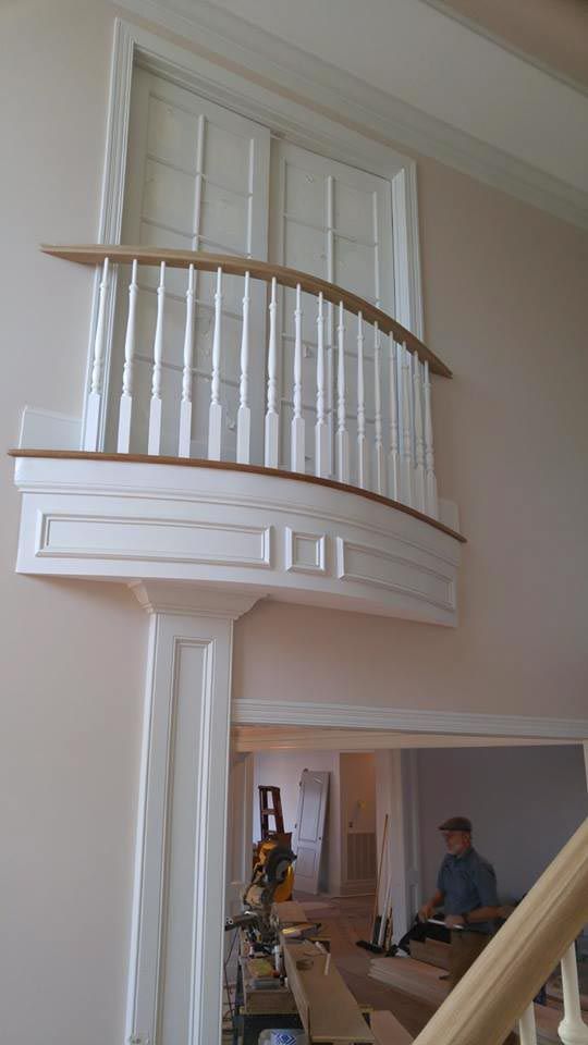 Balcony with white spindles, curved wood handrail, and white molding, overlooking a doorway.