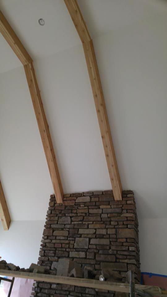 Stone fireplace with wood beams extending to a white, sloped ceiling.
