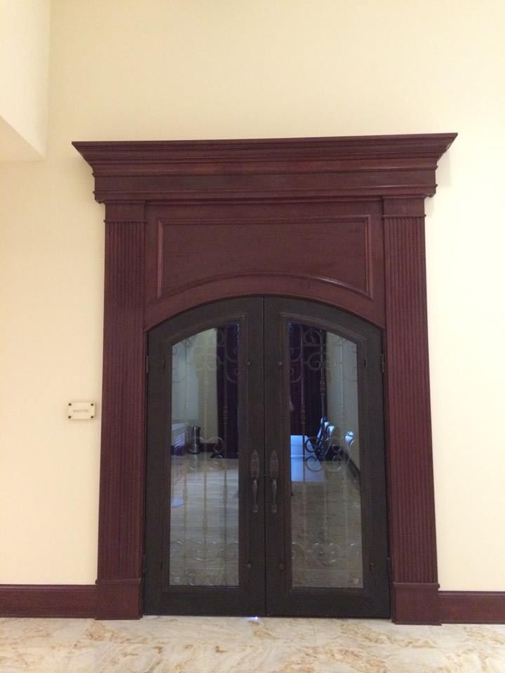 Dark wood double doors with arched glass panels, framed by dark red molding against a cream-colored wall.
