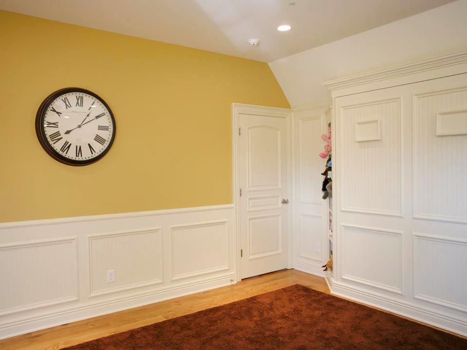Room with yellow walls, white wainscoting, and a large clock; a brown rug and white closet are visible.