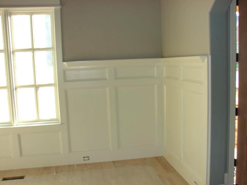 Corner room with white paneled walls, window with sunlight, and wooden floor.