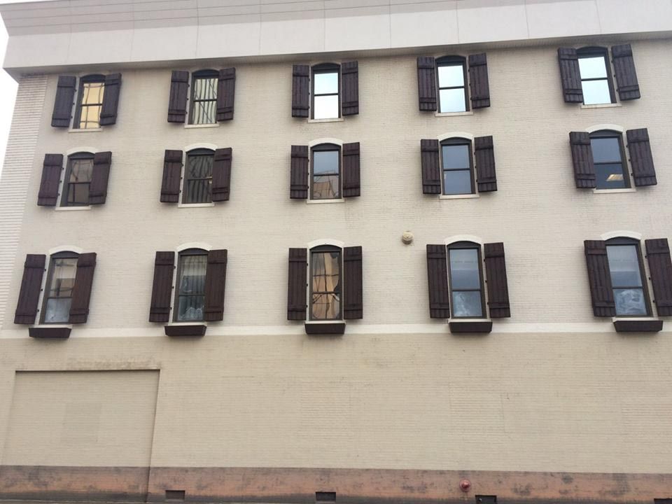 Beige building with three rows of windows, each with brown shutters.