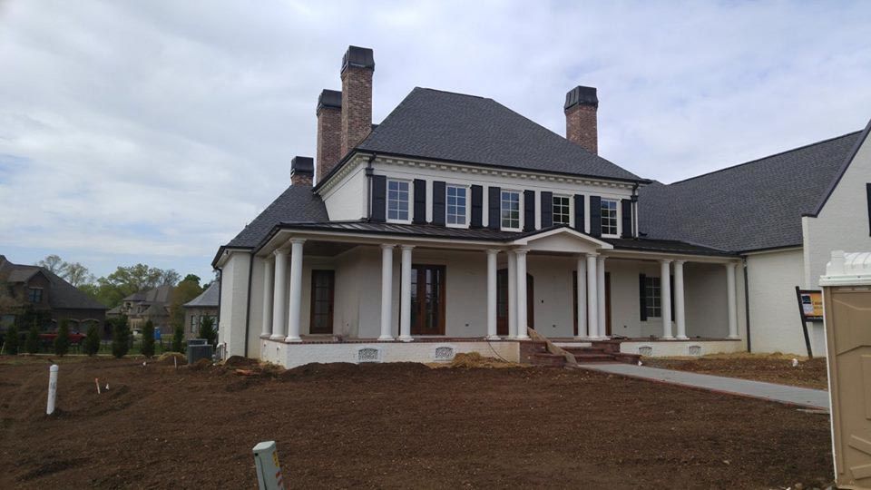 A two-story house under construction with white siding, dark roof, and columns.