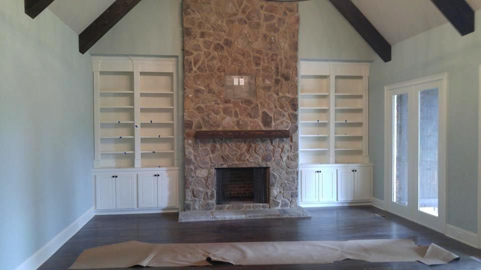 Living room with stone fireplace, built-in white bookshelves, and dark wood floors.