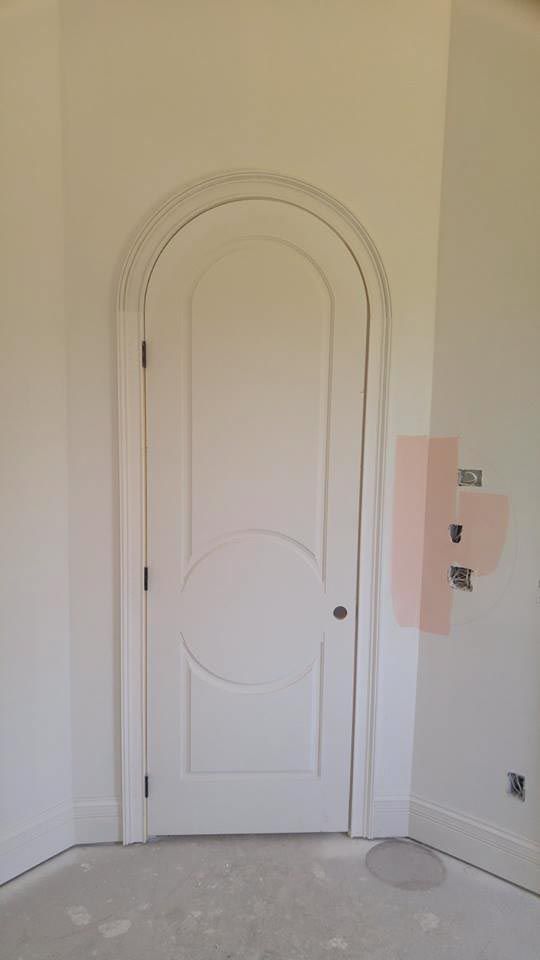 White arched doorway with a circular design, painted walls, unfinished flooring.