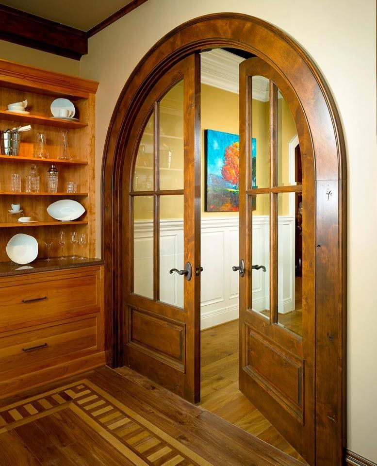Wooden arched double doors with glass panels and a framed painting inside.