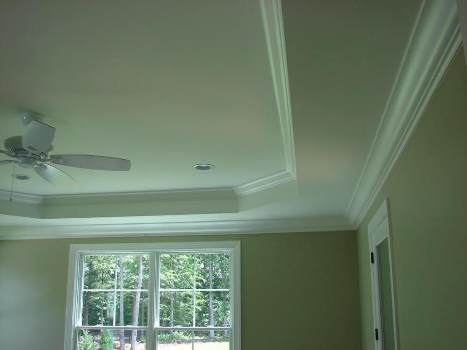 Room interior with white crown molding, recessed ceiling, and window overlooking trees.