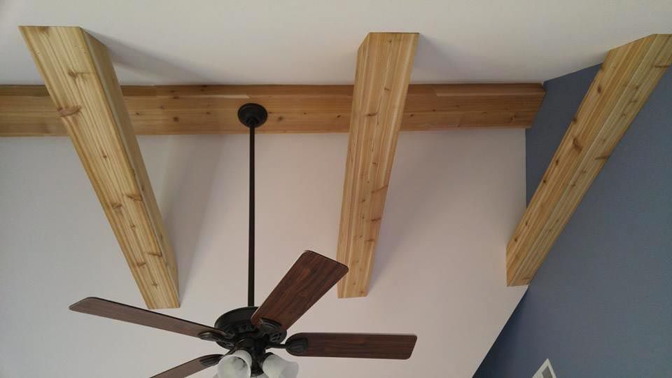 Wooden beams and supports on a white ceiling, with a ceiling fan below and blue wall.