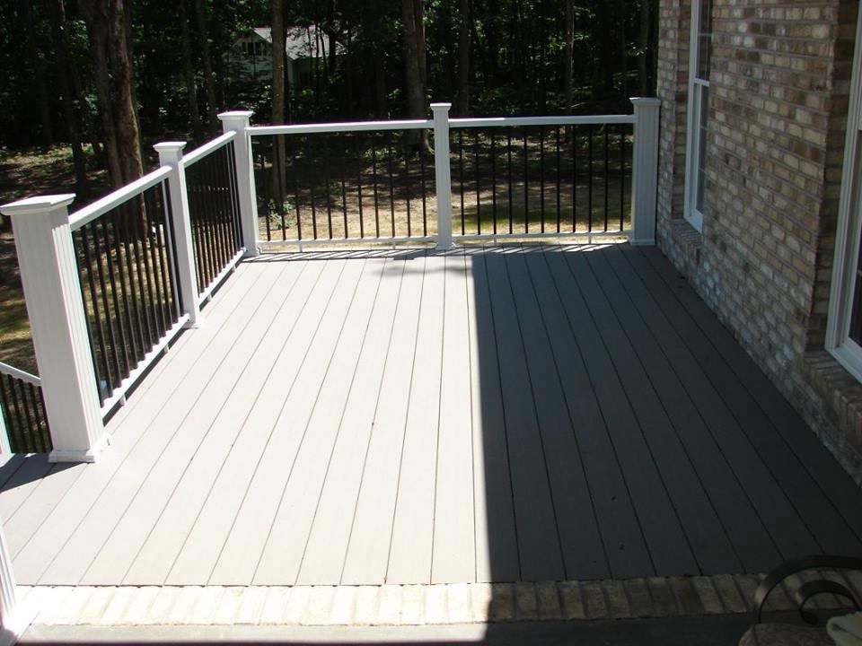 Back deck that has grey deck boards, a white railing, and black iron rods. The deck is attached to a home with tan brick.