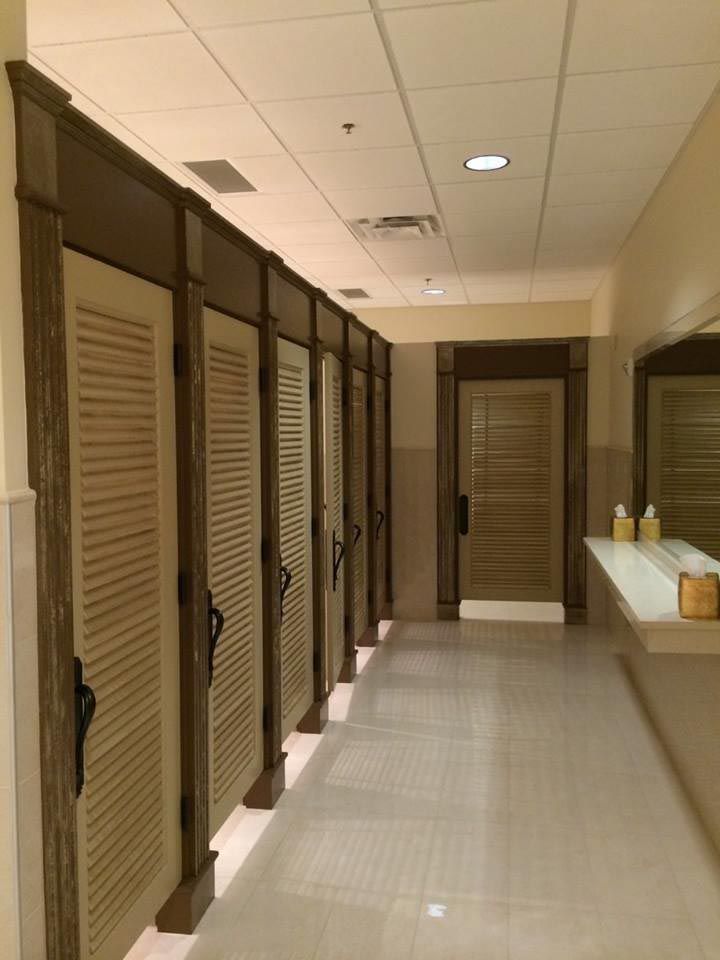 Hallway of restroom stalls with shuttered doors and a mirror.