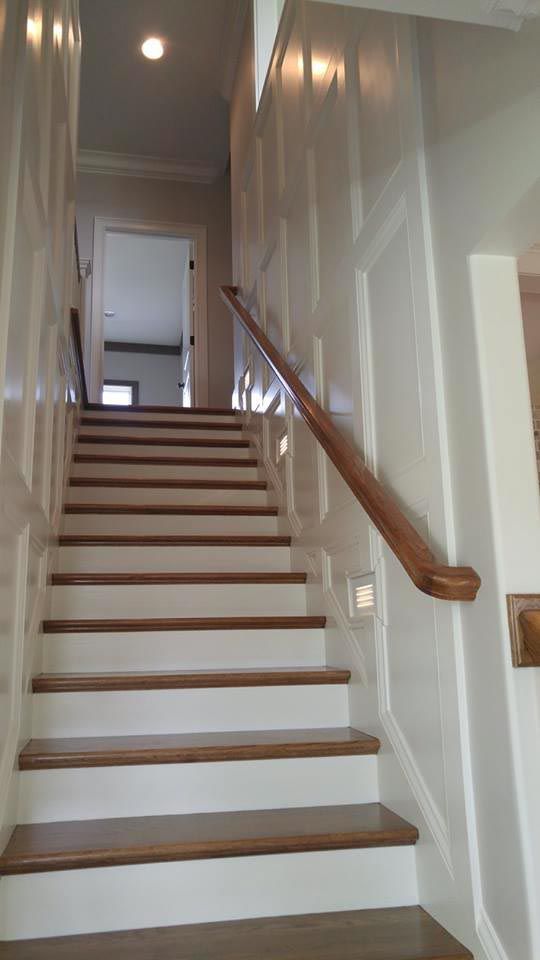 Wooden staircase with white paneling and a dark wood handrail, leading upwards towards a doorway.