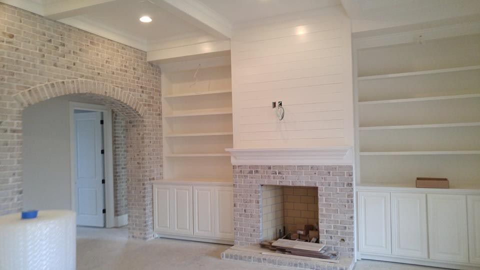 Brick fireplace and archway with built-in white bookshelves. Empty room under construction, with white floors and walls.