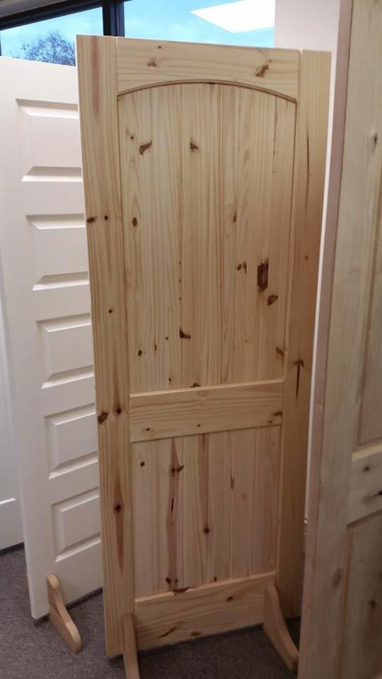 Wooden door with arch top and lower panel, unfinished, on a stand indoors.
