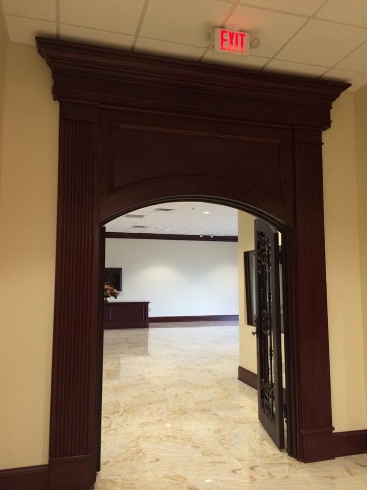 Dark wood arched doorway leading to a brightly lit room with marble flooring. An exit sign is above.